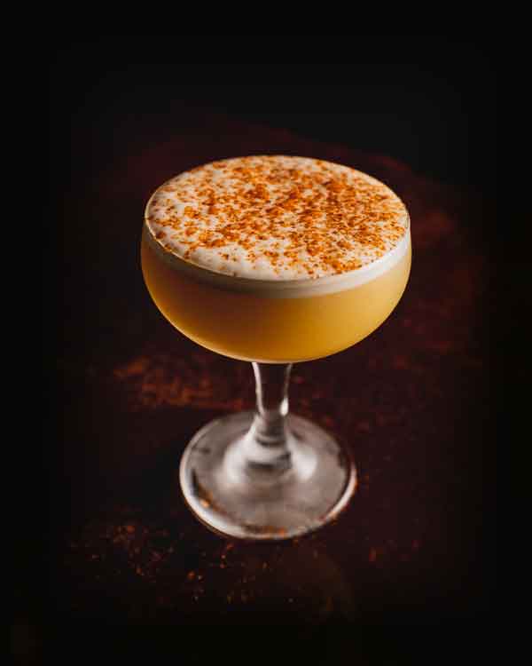 photo of a hand-crafted, orange-colored cocktail with foam on top